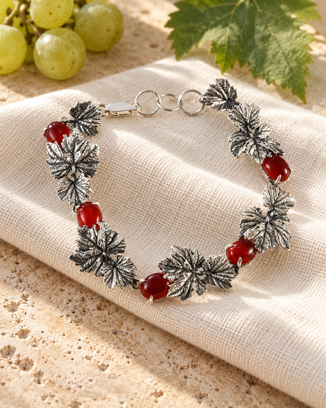 Silver grape vine leaf bracelet with red carnelian stones on travertine and linen
