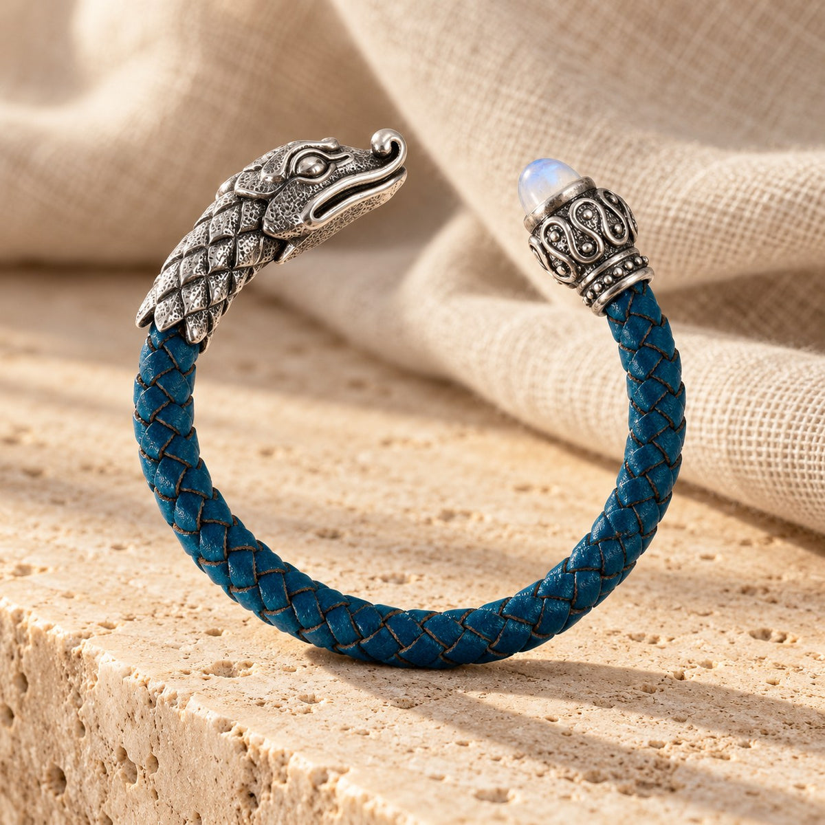 Teal braided leather cuff with a silver crocodile head and a moonstone on travertine