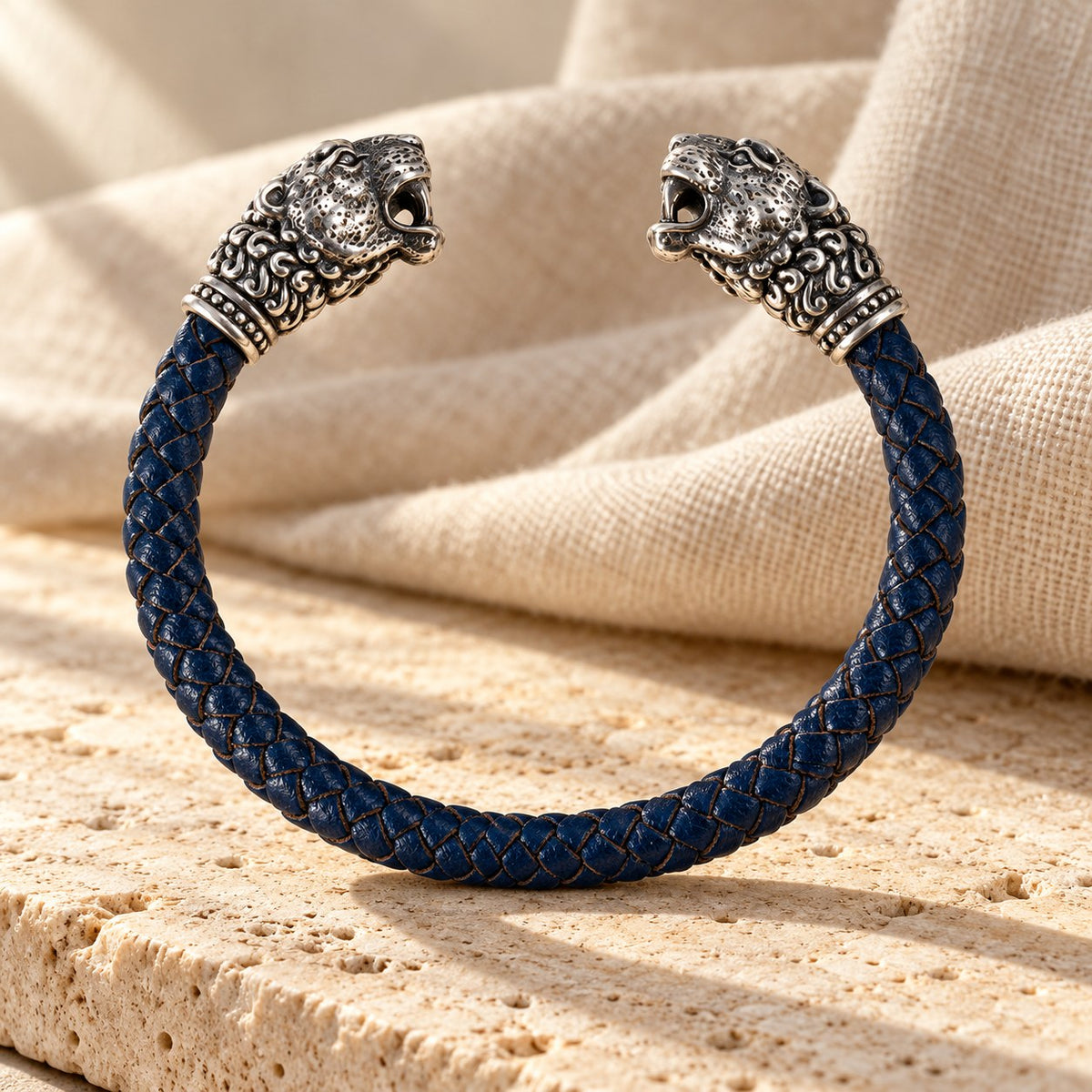 Navy braided leather cuff with two silver snow leopard heads on travertine