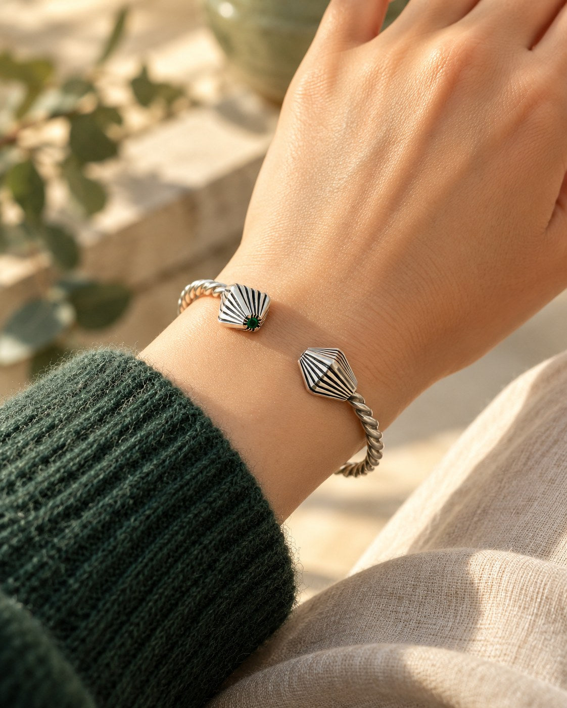 Twisted silver rope cuff with fluted ends worn on a wrist with a green sweater