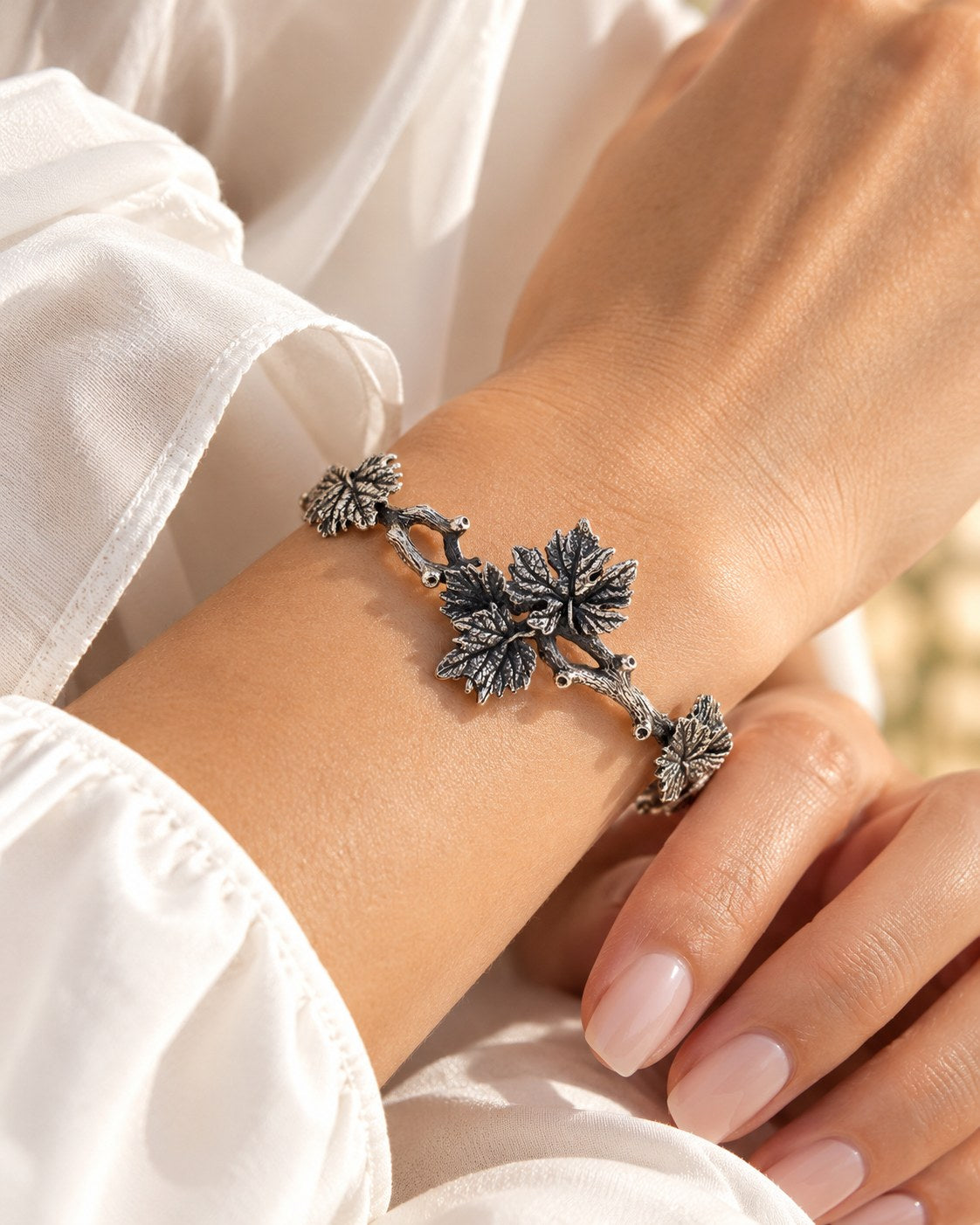 Silver grapevine branch bracelet worn on a woman's wrist with a white silk sleeve