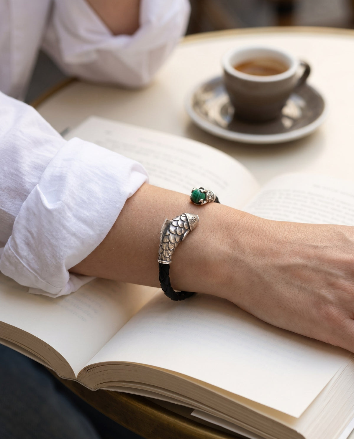 Braided black leather bracelet with a silver carp head and a green stone worn on a wrist