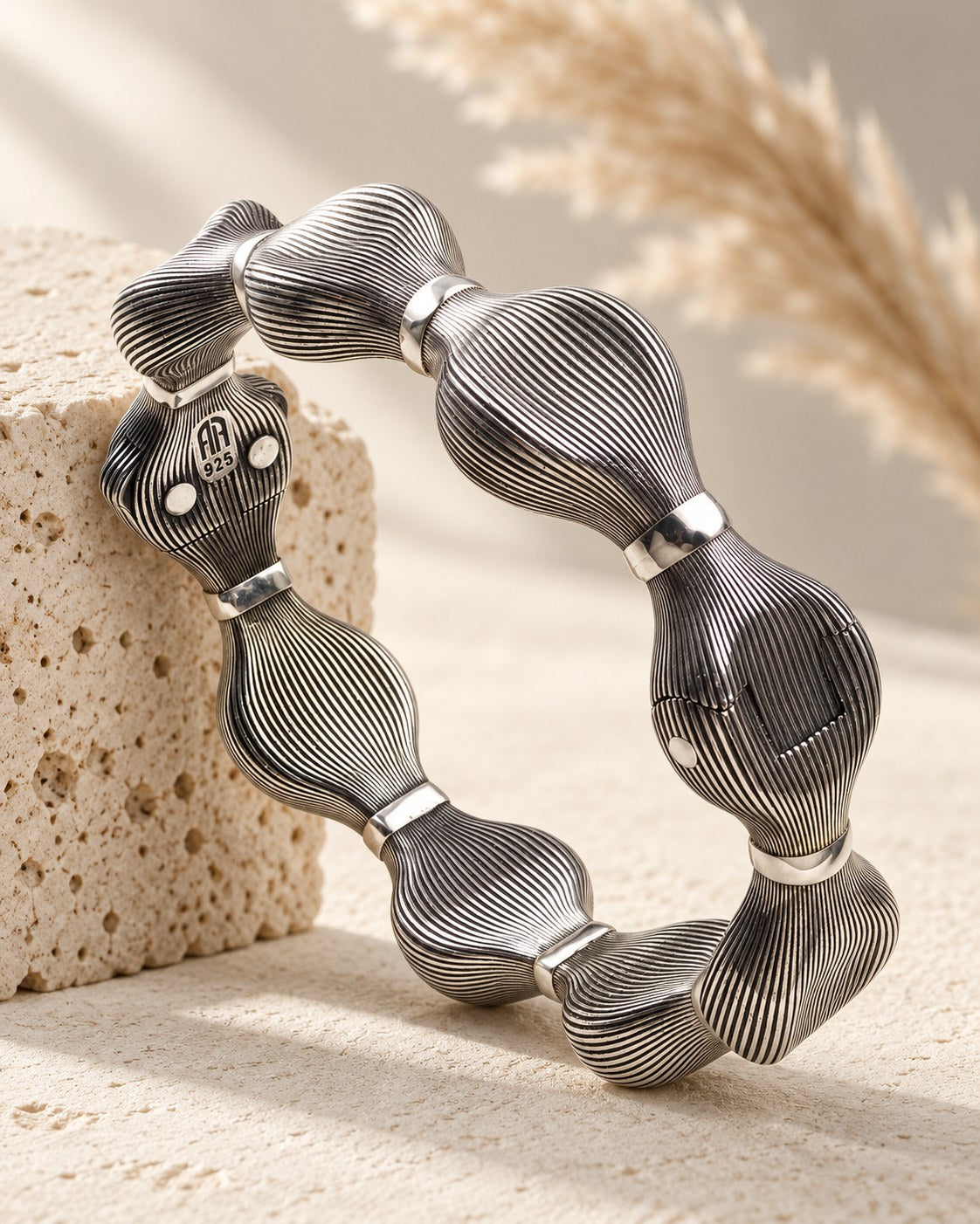 Darkened silver bracelet of ridged pod links on travertine