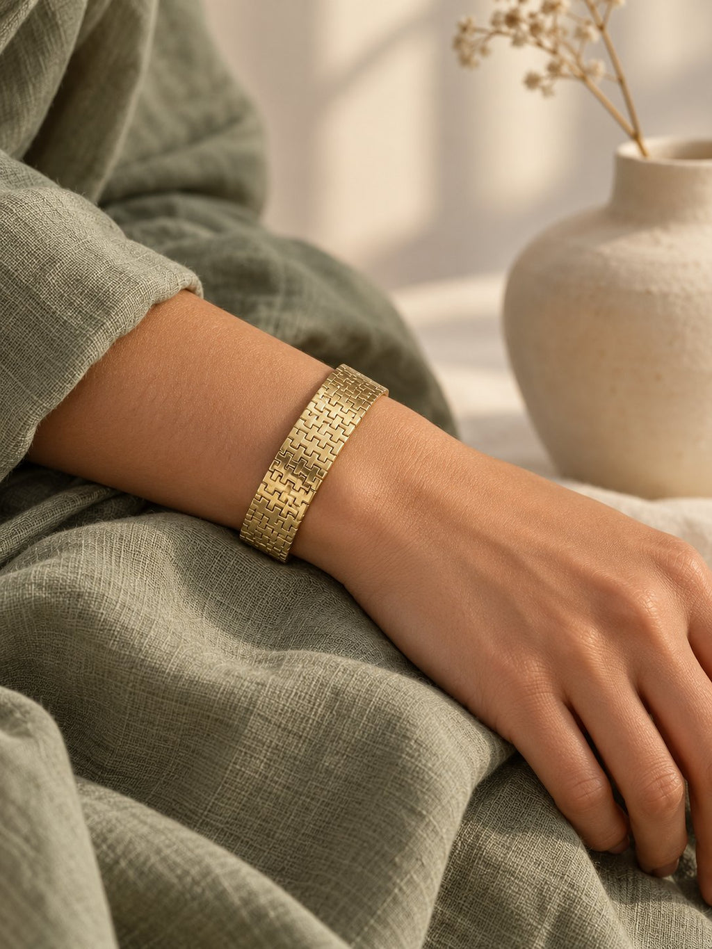 Gold-plated woven link bracelet on the wrist over sage linen