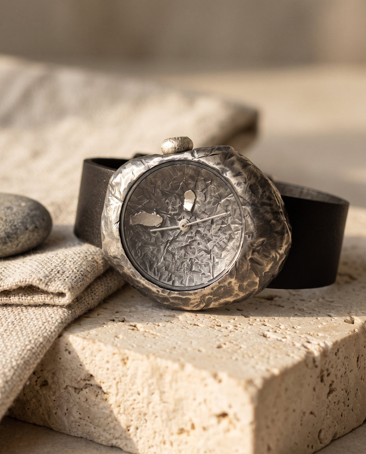 Aurelliani hand-hammered sterling silver watch with black leather strap on travertine