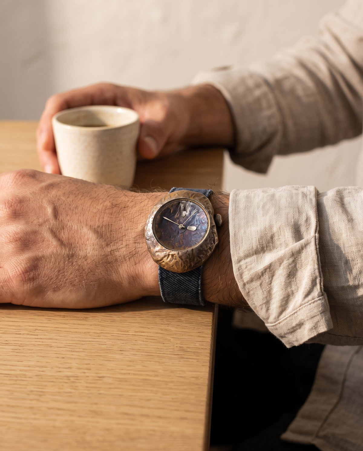 Aurelliani hammered bronze watch with indigo strap worn on a man's wrist