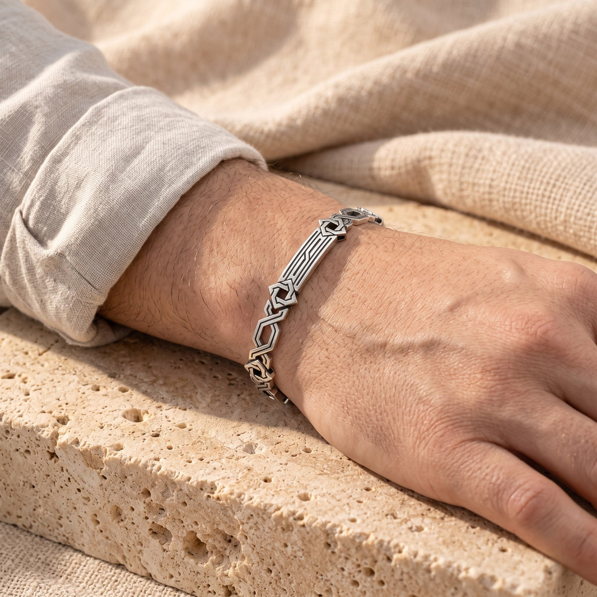Silver geometric link bracelet worn on a wrist resting on stone