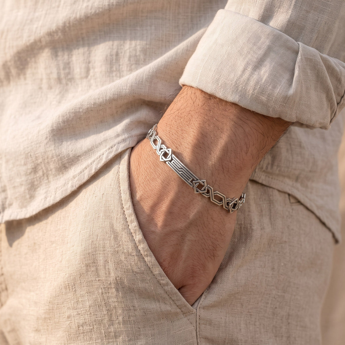 Sterling silver ornament bracelet on a wrist with linen trousers
