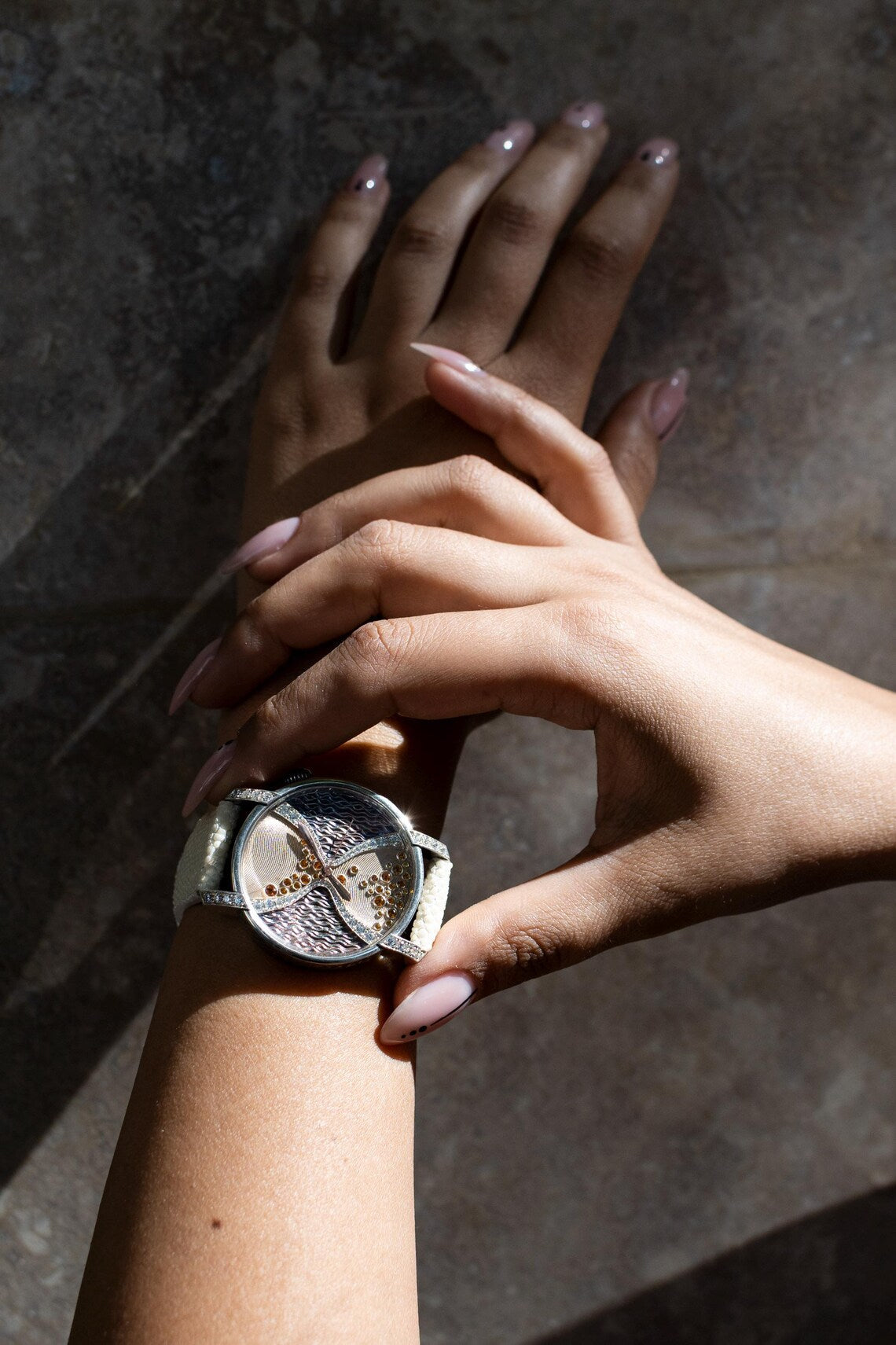Silver watch worn with crossed hands against warm stone