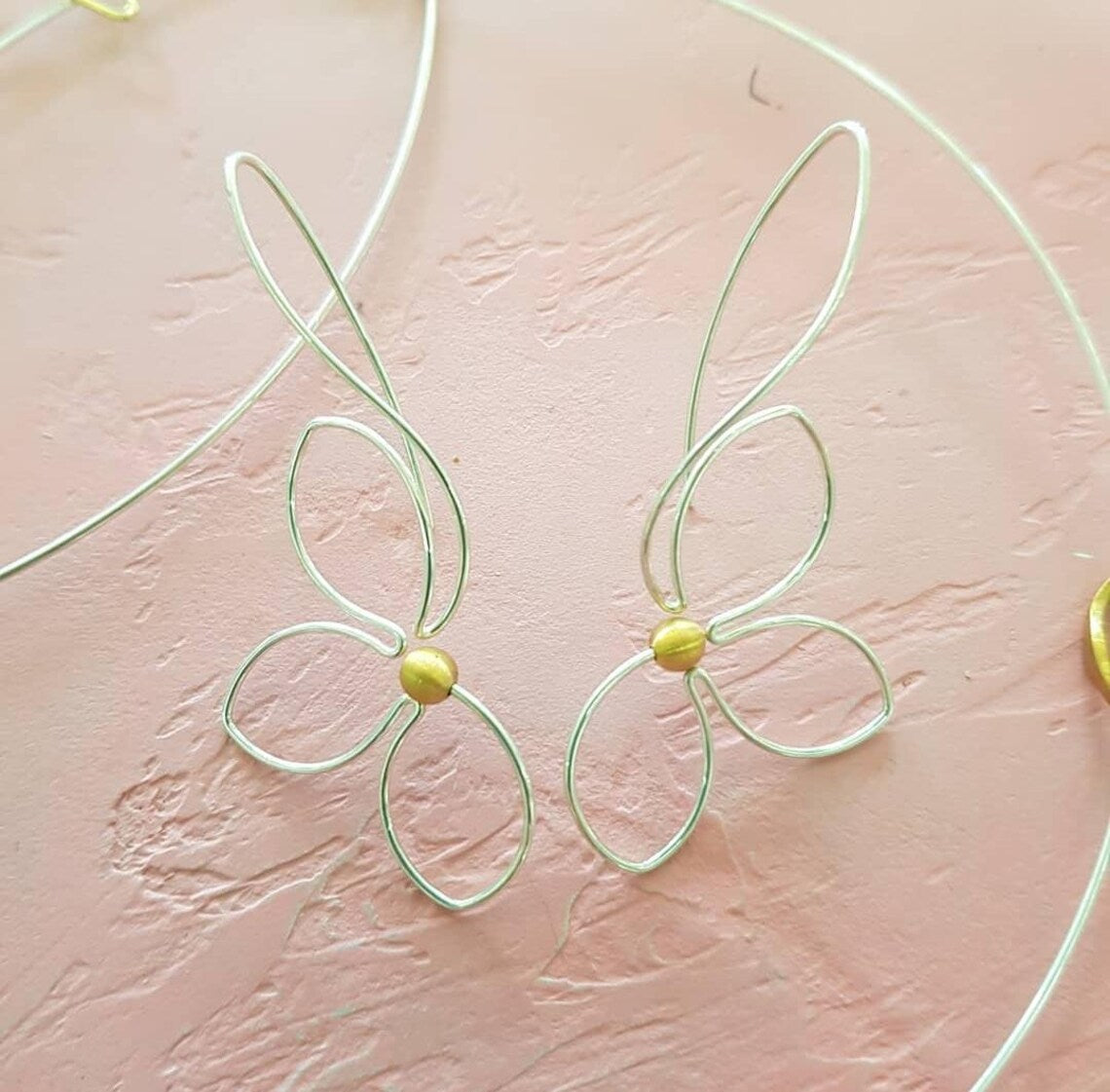 Pair of silver flower wire earrings with pearls on a blush plaster background
