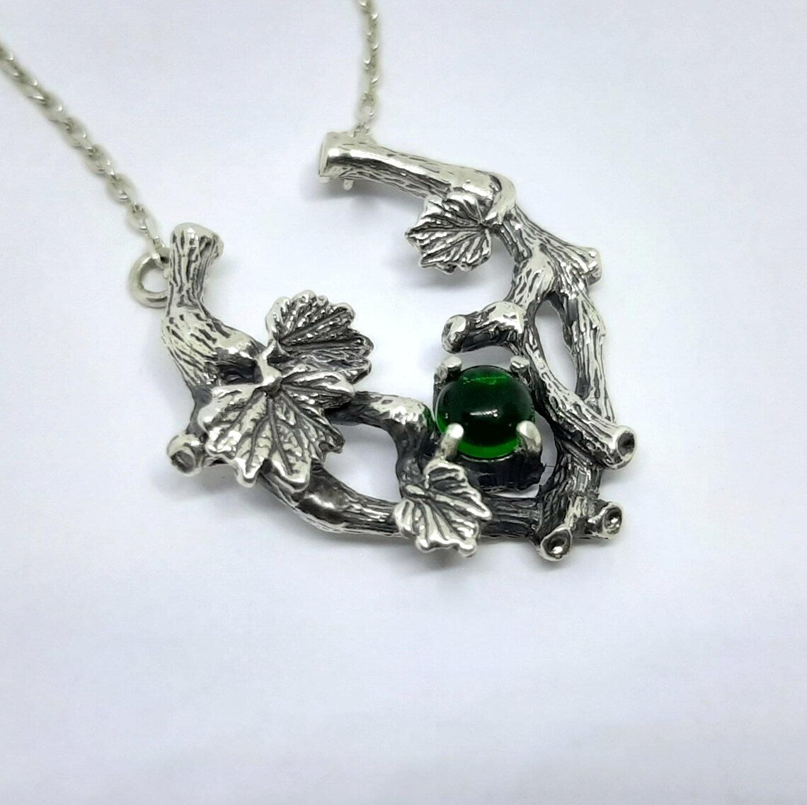 Close view of the silver grape vine pendant with leaves and a round green stone