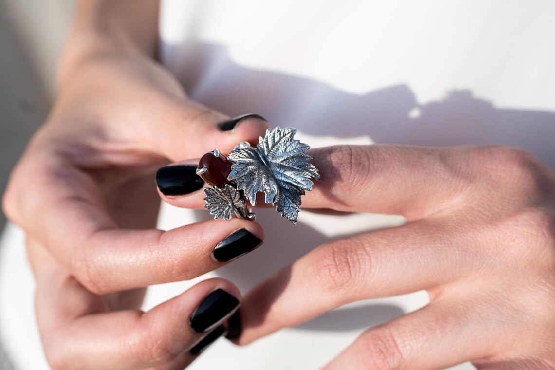 Hands holding the silver vine leaf ring with a red carnelian stone