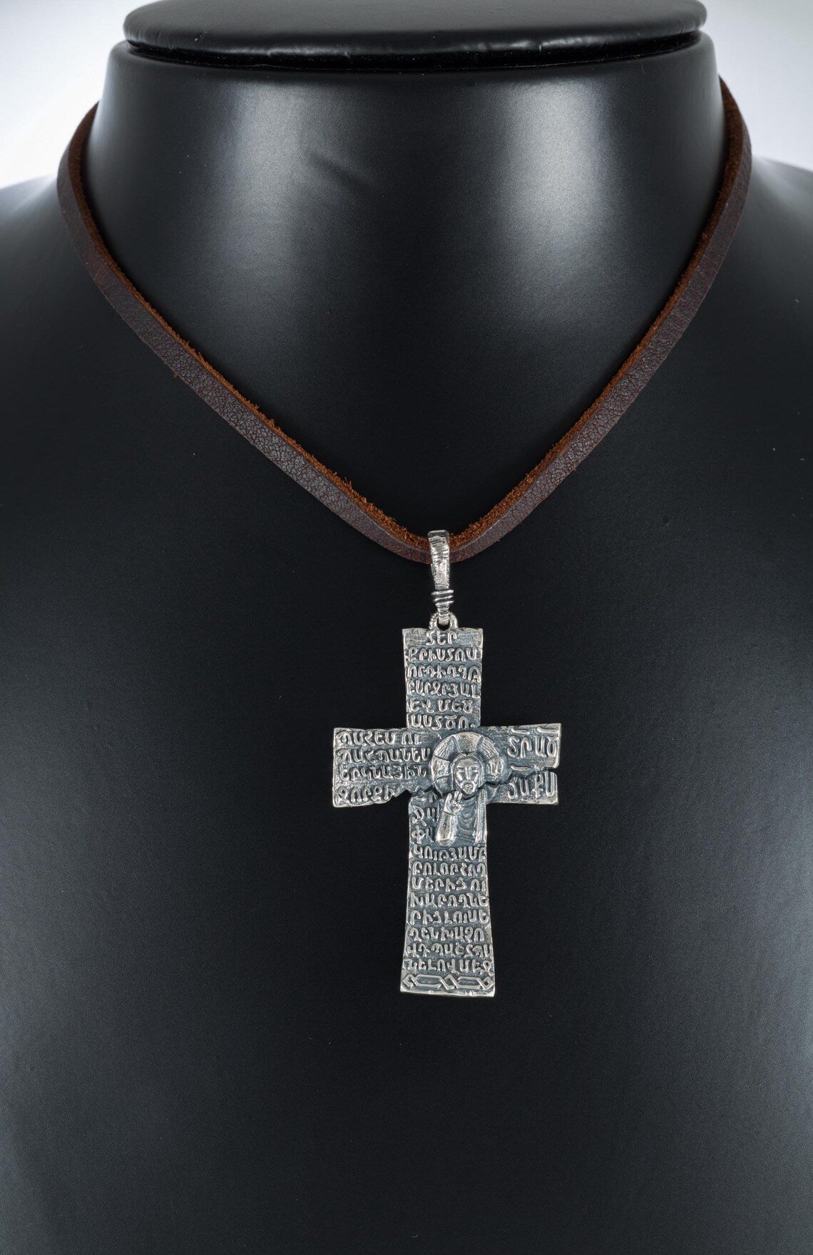 Oxidized silver cross pendant with Armenian letters on a display bust