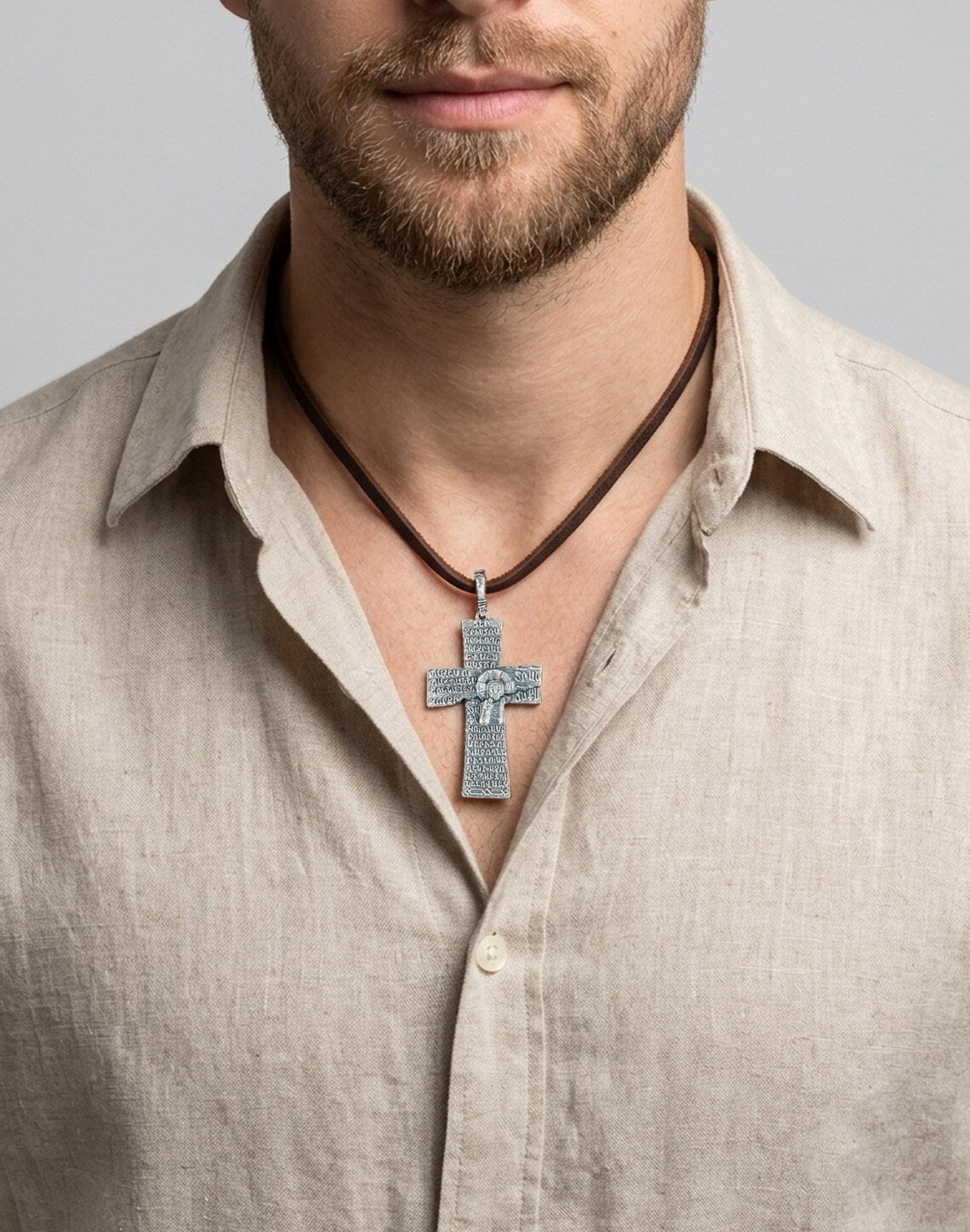 Silver Armenian cross pendant on a leather cord worn with a linen shirt